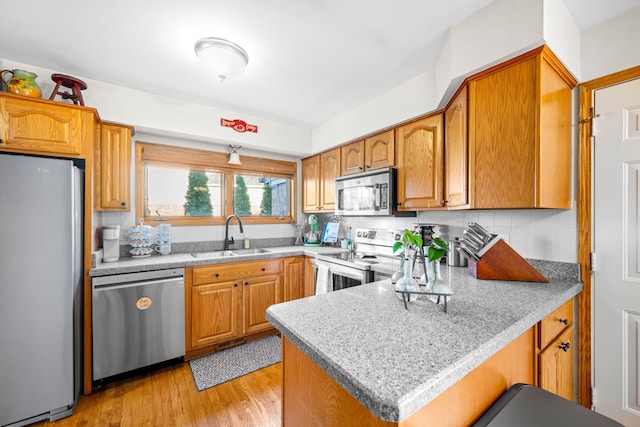 kitchen featuring light wood finished floors, backsplash, appliances with stainless steel finishes, a peninsula, and a sink