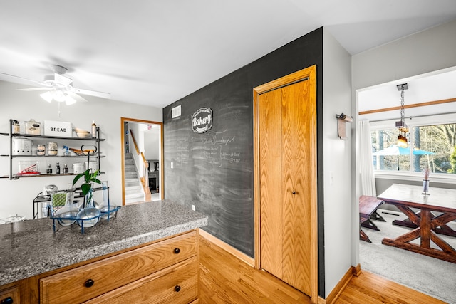 kitchen with light wood-type flooring, baseboards, a ceiling fan, and brown cabinetry