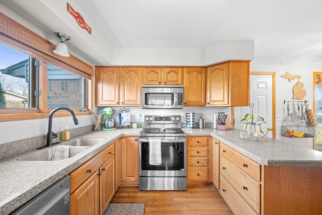 kitchen with a peninsula, a sink, stainless steel appliances, light countertops, and light wood-type flooring