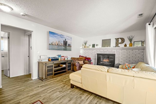 living room featuring a fireplace, a textured ceiling, baseboards, and wood finished floors