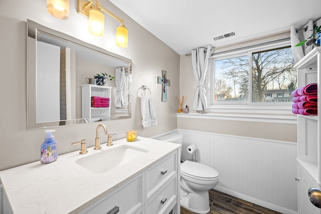 bathroom featuring visible vents, a wainscoted wall, toilet, wood finished floors, and vanity