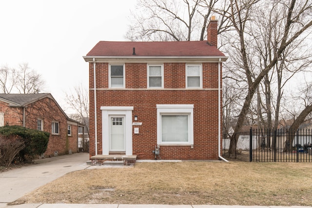 view of front of property with brick siding, a chimney, a front lawn, and fence