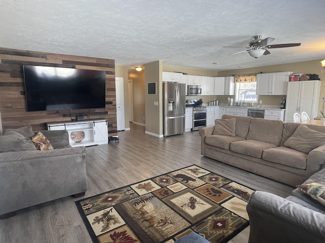 living area featuring baseboards, a textured ceiling, ceiling fan, and light wood finished floors