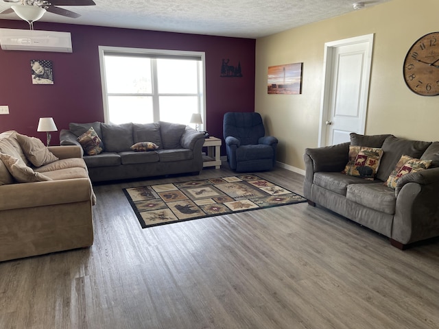 living area featuring a textured ceiling, an AC wall unit, wood finished floors, and a ceiling fan