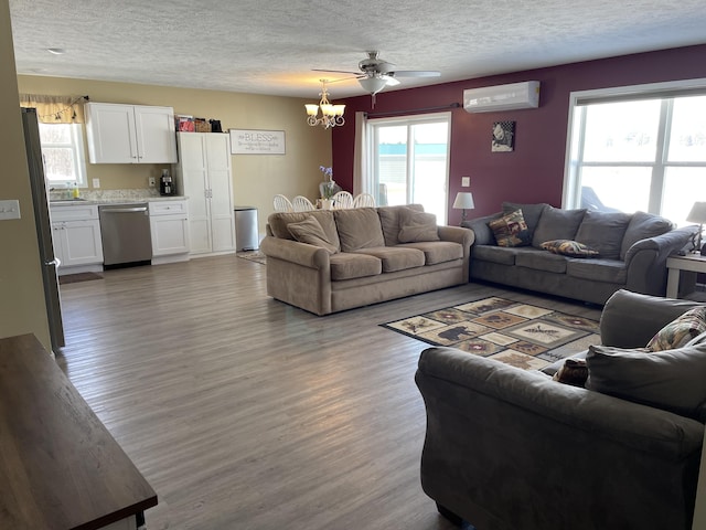 living room with ceiling fan with notable chandelier, a textured ceiling, wood finished floors, and a wall mounted AC