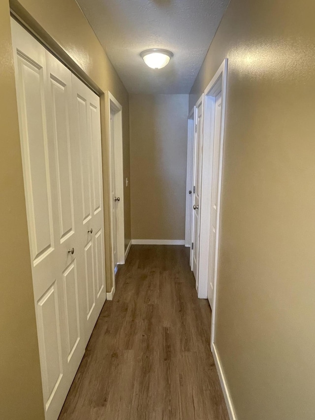 hall with baseboards, dark wood-type flooring, and a textured ceiling