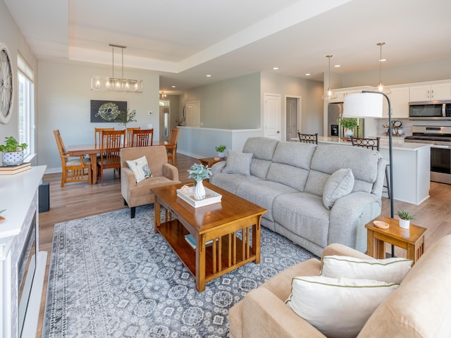 living room featuring recessed lighting, light wood-type flooring, a raised ceiling, and baseboards