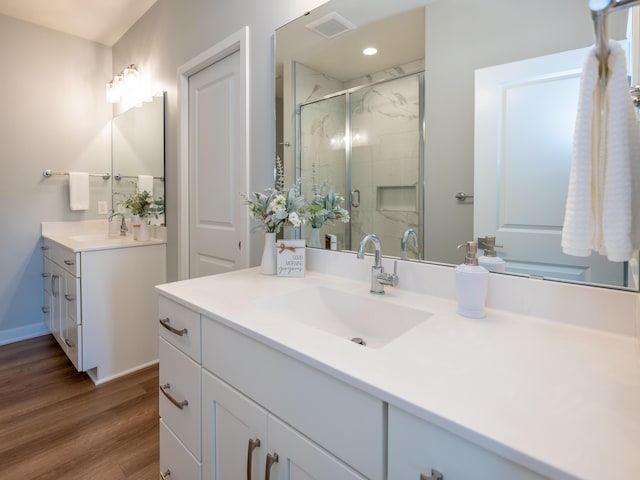 bathroom featuring visible vents, two vanities, a sink, wood finished floors, and a shower stall