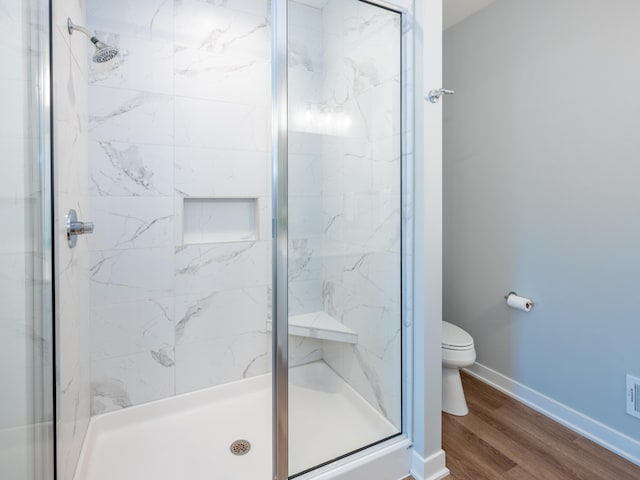 bathroom with a shower stall, toilet, wood finished floors, and baseboards