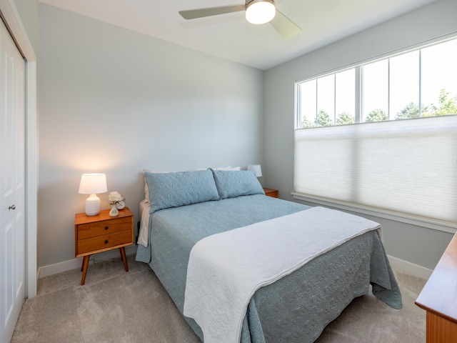 bedroom featuring light carpet, ceiling fan, baseboards, and a closet