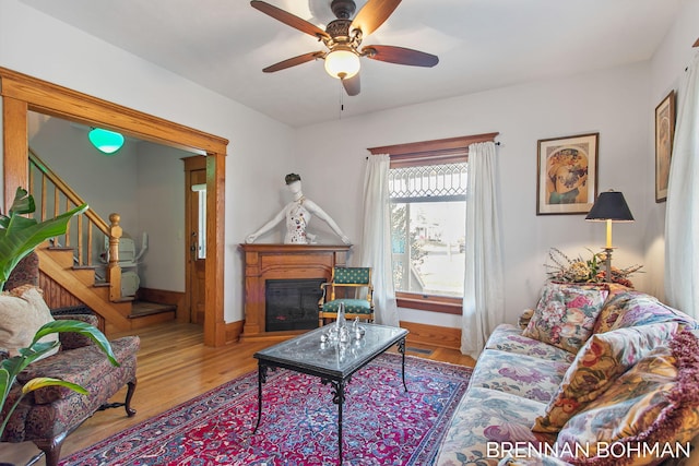 living room featuring visible vents, a ceiling fan, a glass covered fireplace, wood finished floors, and stairway