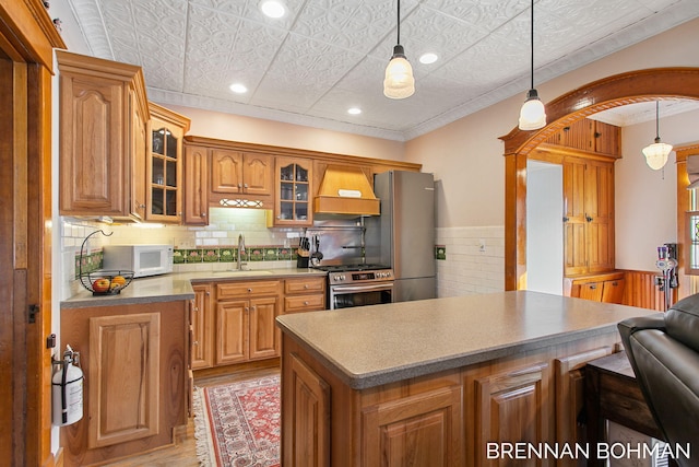 kitchen featuring custom range hood, arched walkways, an ornate ceiling, stainless steel appliances, and a sink