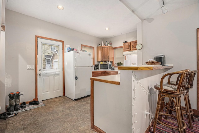 kitchen featuring stainless steel microwave, recessed lighting, brown cabinets, a peninsula, and freestanding refrigerator