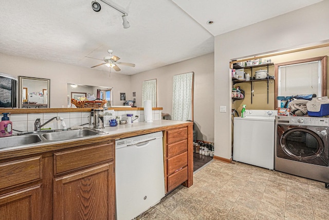 kitchen with dishwasher, washing machine and clothes dryer, brown cabinets, and a sink