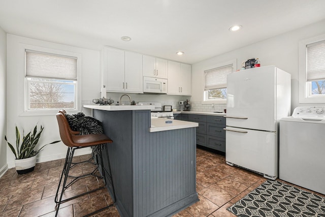 kitchen featuring a kitchen bar, white appliances, plenty of natural light, and washer / dryer