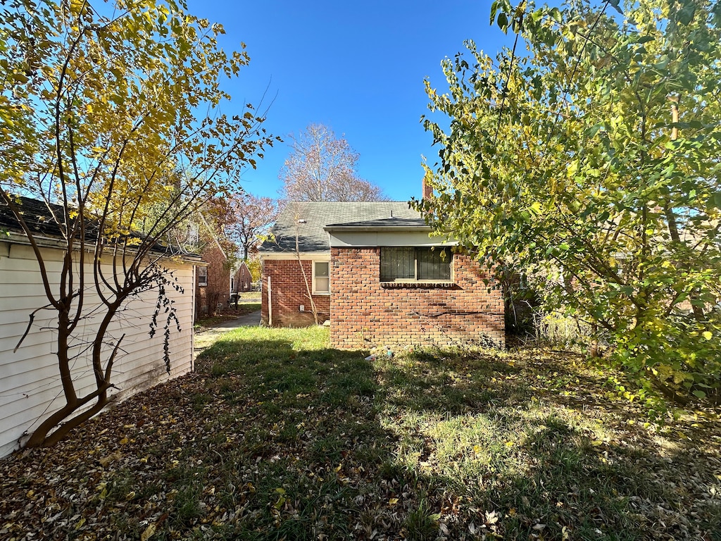 rear view of house featuring brick siding, a lawn, and roof with shingles