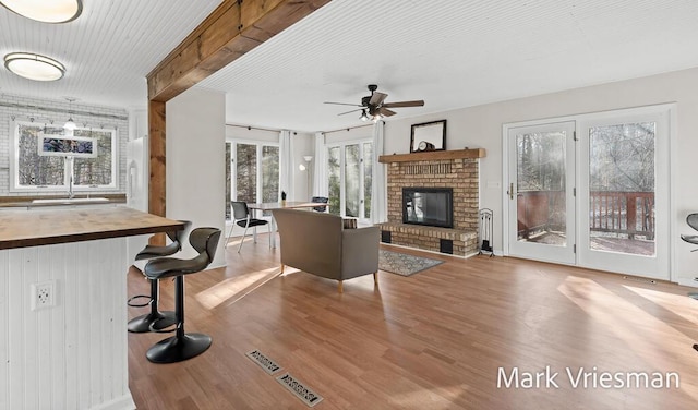 living room with a ceiling fan, a brick fireplace, wood finished floors, and visible vents