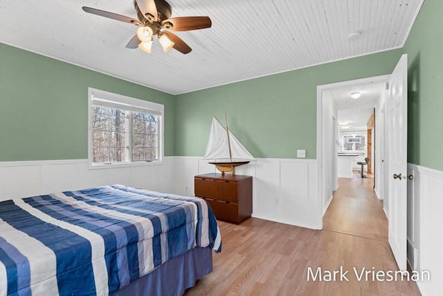 bedroom with a ceiling fan, wood ceiling, wood finished floors, and wainscoting