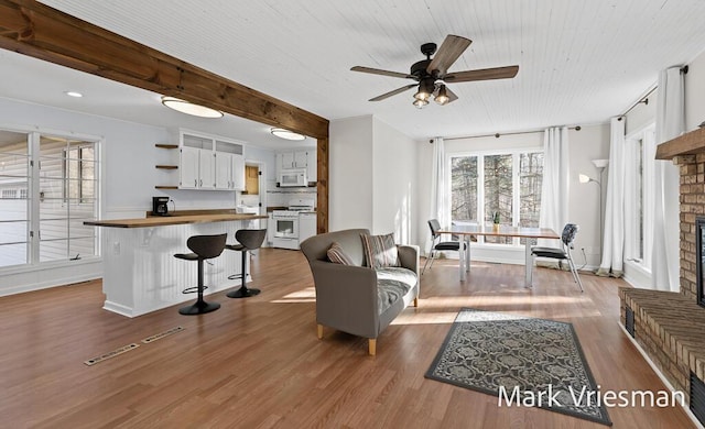 living area featuring baseboards, beamed ceiling, a fireplace, wood finished floors, and a ceiling fan