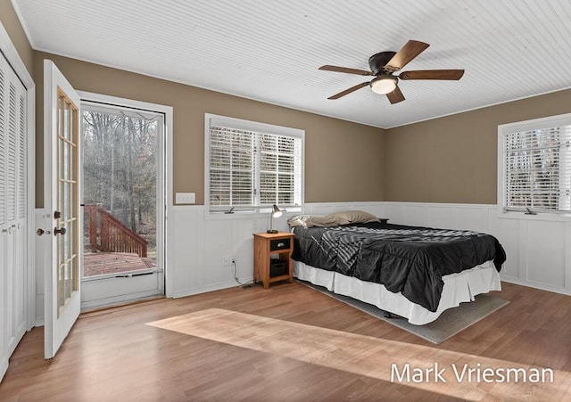 bedroom featuring a wainscoted wall, wood finished floors, a ceiling fan, and access to outside