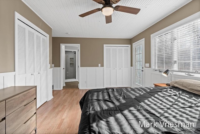 bedroom featuring a wainscoted wall, two closets, a ceiling fan, light wood finished floors, and wood ceiling