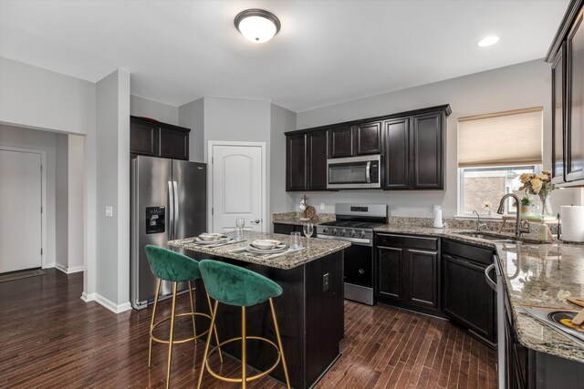 kitchen featuring dark wood-style flooring, stainless steel appliances, light stone countertops, a sink, and a kitchen island with sink