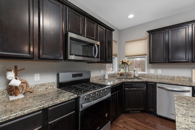 kitchen featuring dark wood-style floors, a sink, light stone counters, and appliances with stainless steel finishes