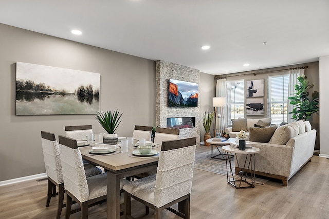 dining room featuring recessed lighting, light wood-type flooring, baseboards, and a stone fireplace