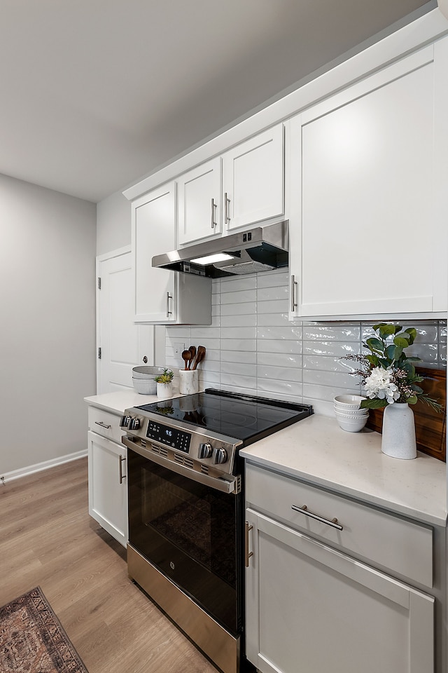 kitchen with under cabinet range hood, tasteful backsplash, light wood-style floors, stainless steel electric range, and white cabinets