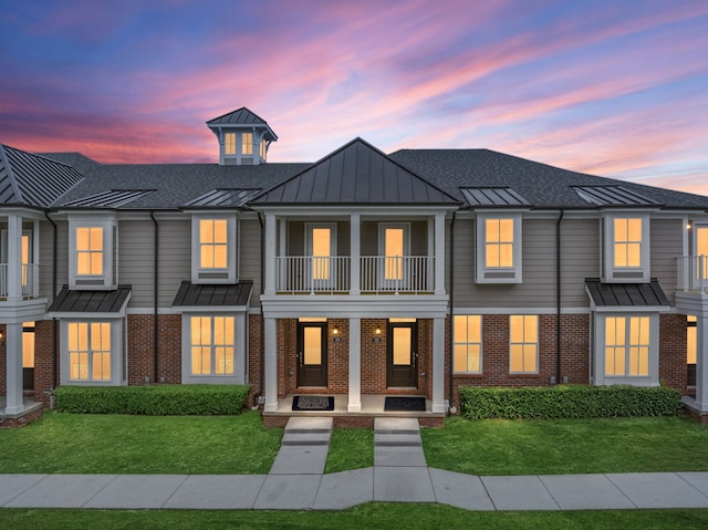 townhome / multi-family property featuring a standing seam roof, a balcony, a front yard, metal roof, and brick siding