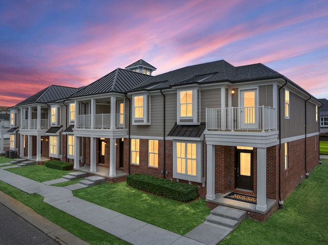 view of property featuring brick siding, central AC unit, a front lawn, and a balcony