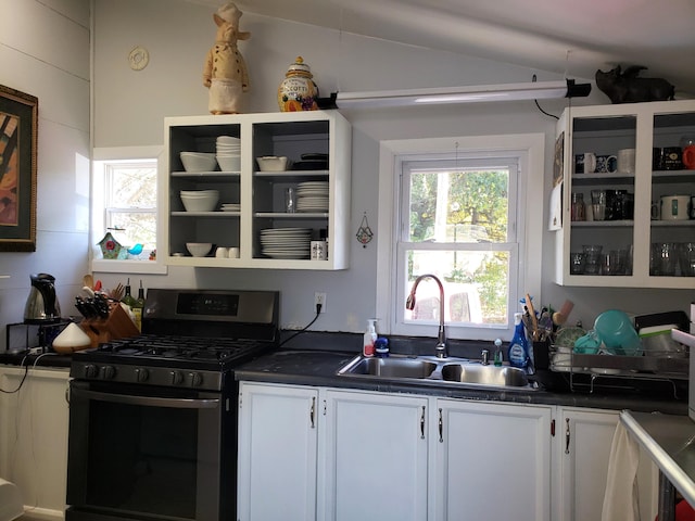 kitchen featuring stainless steel gas range oven, dark countertops, vaulted ceiling, and a sink