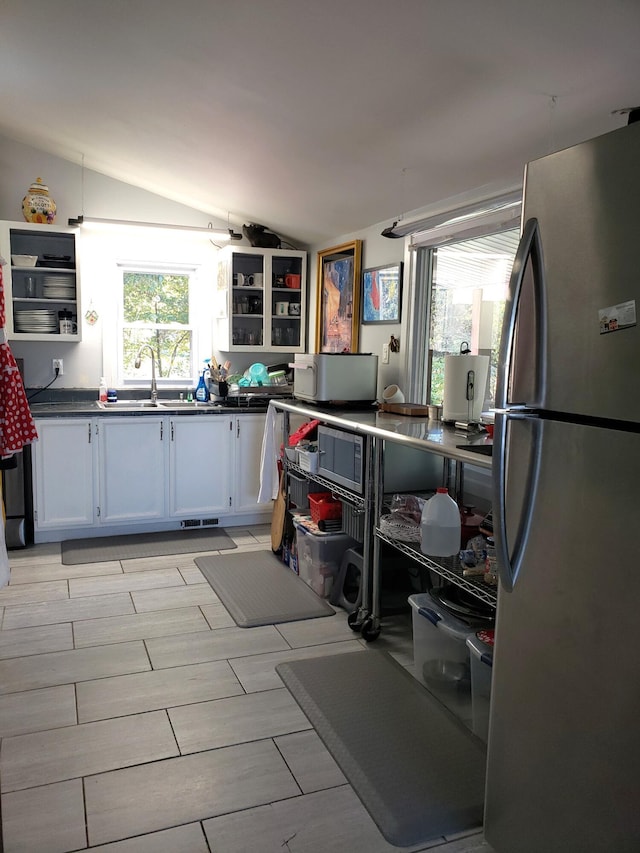 kitchen featuring dark countertops, a healthy amount of sunlight, lofted ceiling, freestanding refrigerator, and a sink