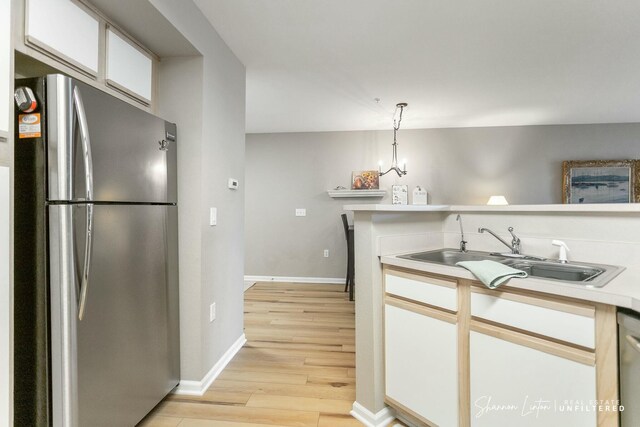 kitchen featuring light wood-style flooring, a sink, freestanding refrigerator, white cabinets, and light countertops