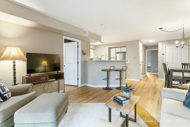 living room featuring visible vents, baseboards, a notable chandelier, and light wood-style flooring