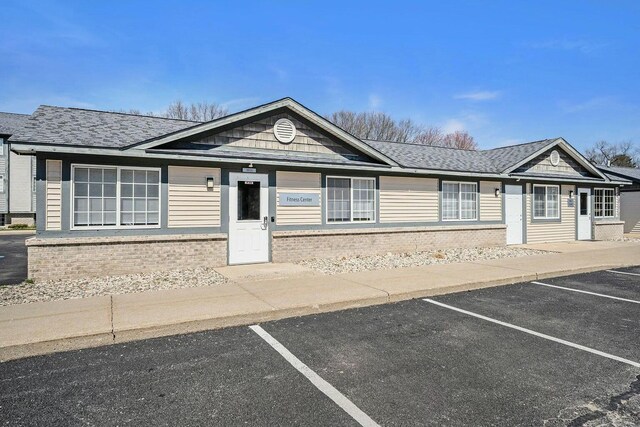 ranch-style house with brick siding, uncovered parking, and roof with shingles