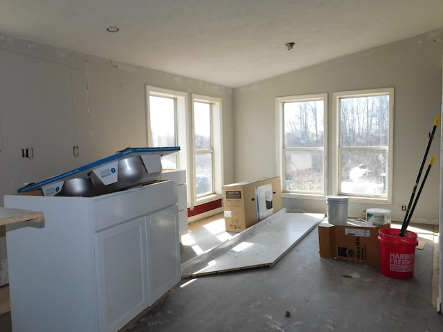 interior space with a wealth of natural light, white cabinets, concrete floors, and lofted ceiling