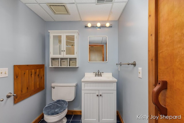 half bathroom featuring vanity, baseboards, visible vents, a drop ceiling, and toilet