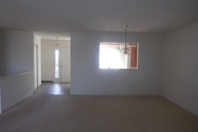 carpeted spare room featuring plenty of natural light and a chandelier