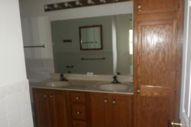 full bathroom with double vanity, tile walls, and a sink