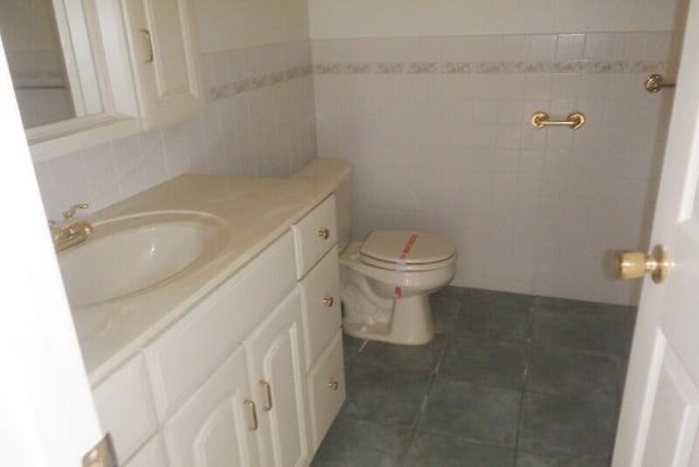 half bath with tile patterned flooring, toilet, vanity, and tile walls