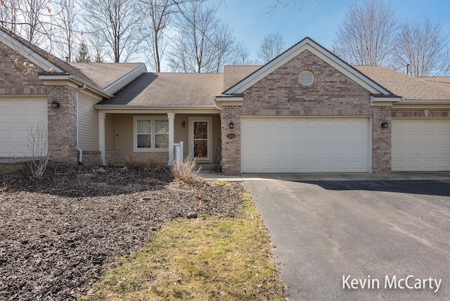 ranch-style house featuring brick siding, driveway, a garage, and roof with shingles