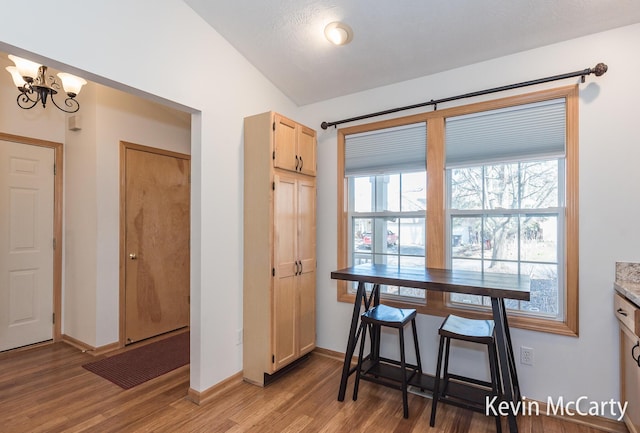 dining room featuring light wood finished floors, baseboards, an inviting chandelier, and vaulted ceiling