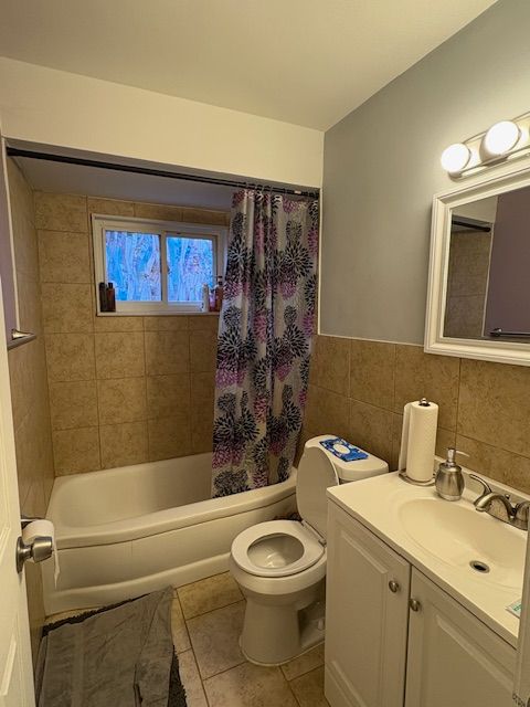 bathroom with toilet, shower / tub combo with curtain, tile walls, tile patterned flooring, and vanity