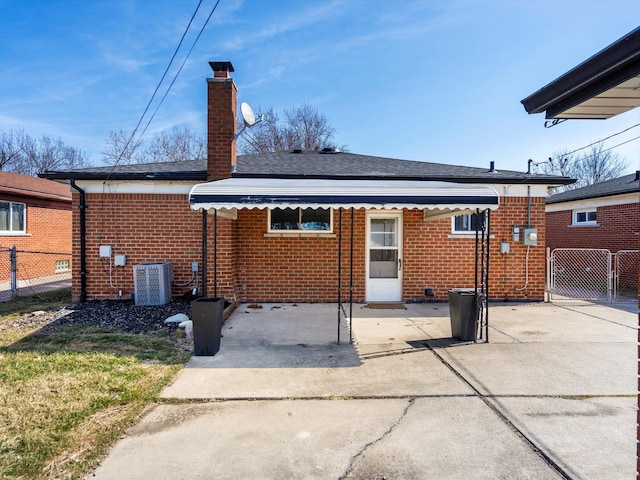 back of property with brick siding, fence, central air condition unit, a chimney, and a gate