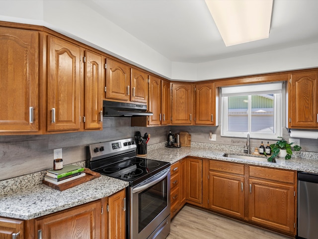 kitchen with under cabinet range hood, light stone counters, brown cabinets, stainless steel appliances, and a sink