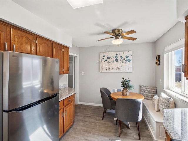 kitchen featuring brown cabinetry, light wood-type flooring, freestanding refrigerator, and ceiling fan