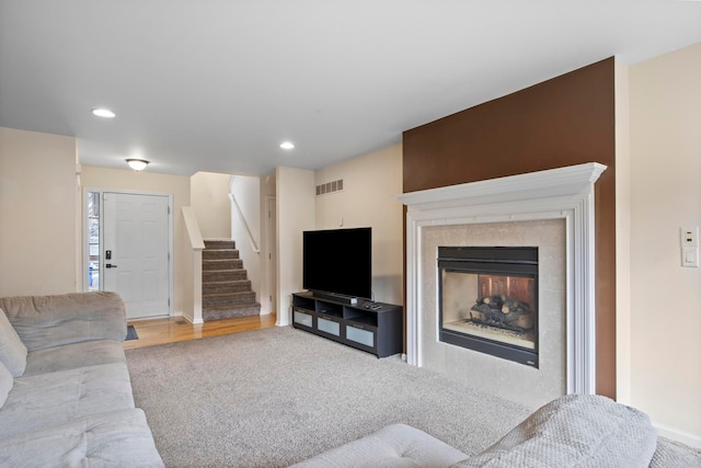 carpeted living room featuring a tiled fireplace, stairway, recessed lighting, and visible vents