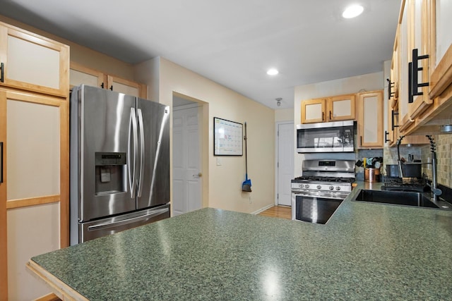 kitchen featuring a sink, tasteful backsplash, dark countertops, appliances with stainless steel finishes, and a peninsula