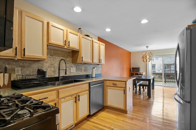 kitchen featuring a sink, appliances with stainless steel finishes, a peninsula, light wood finished floors, and decorative backsplash